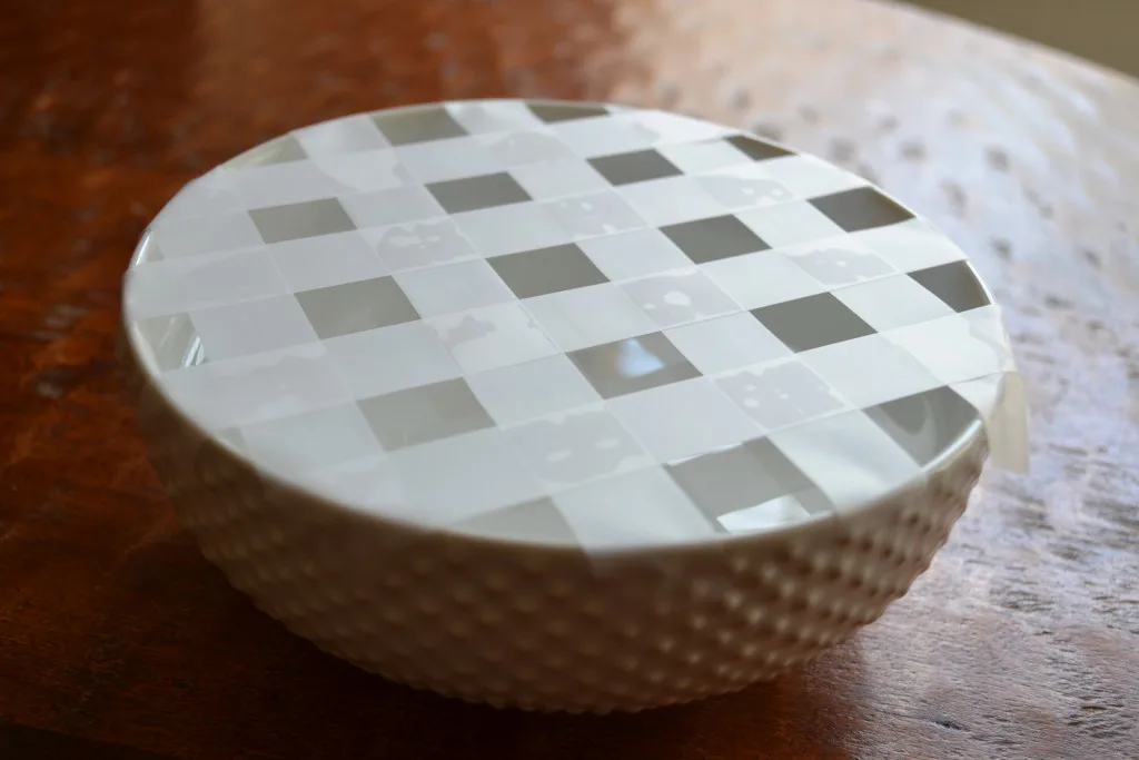 A white bowl with a lattice pattern of tape over the top, used to hold flowers in place.