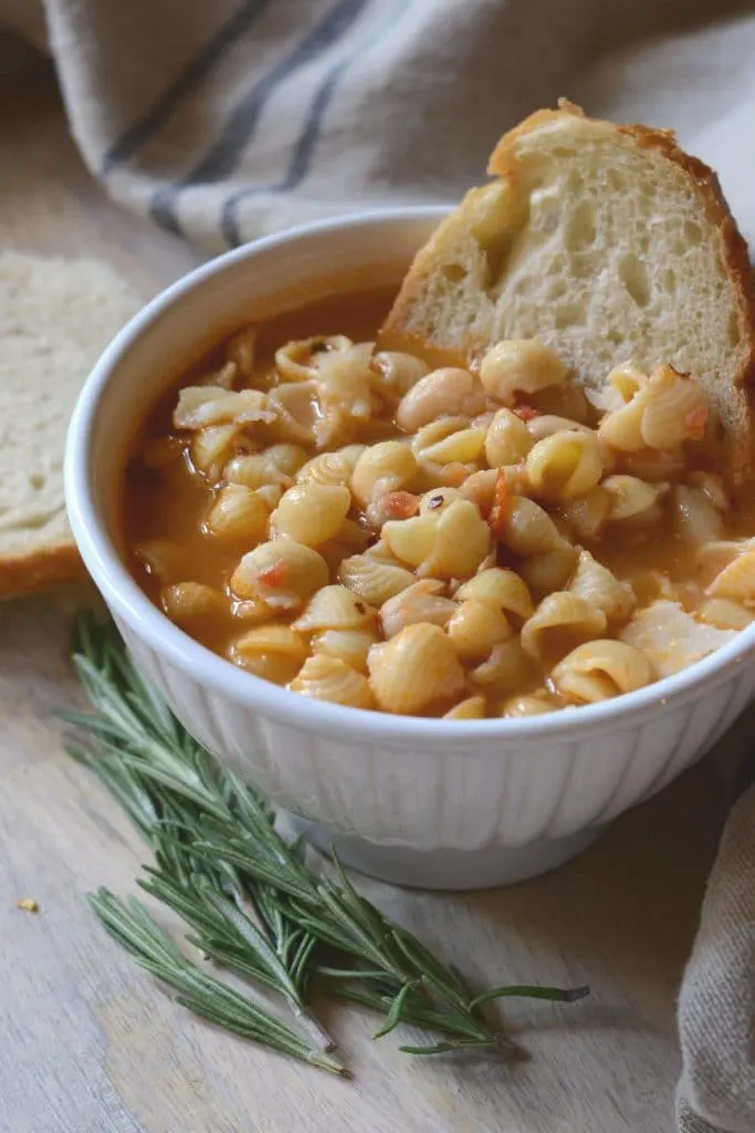 Bowl of pasta e fagioli on a tray with rosemary and crusty bread