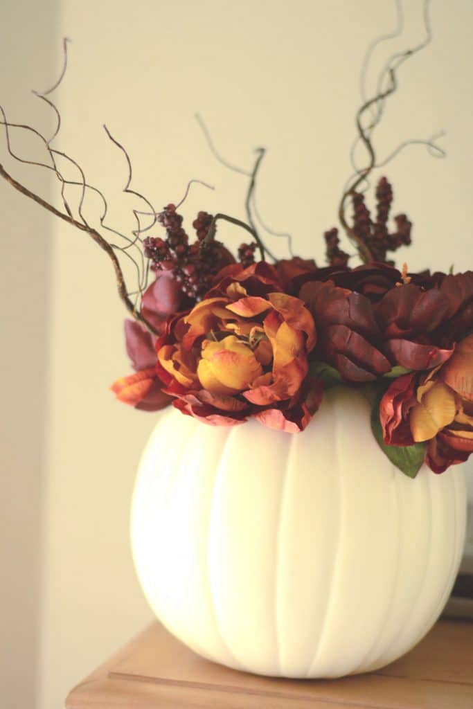 Faux flowers and stems in a vase made from a white craft pumpkin.
