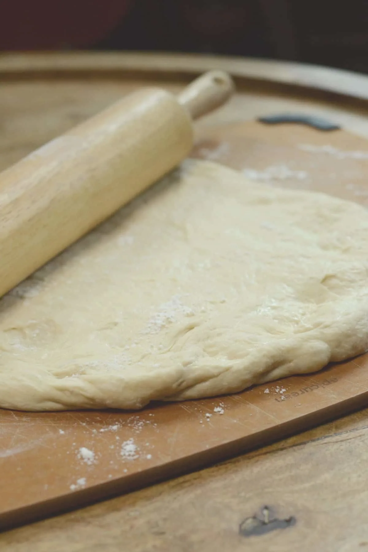 Rolled out pizza dough on a cutting board.