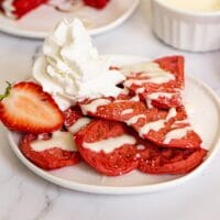 Heart shaped red waffles with whipped cream and strawberries.