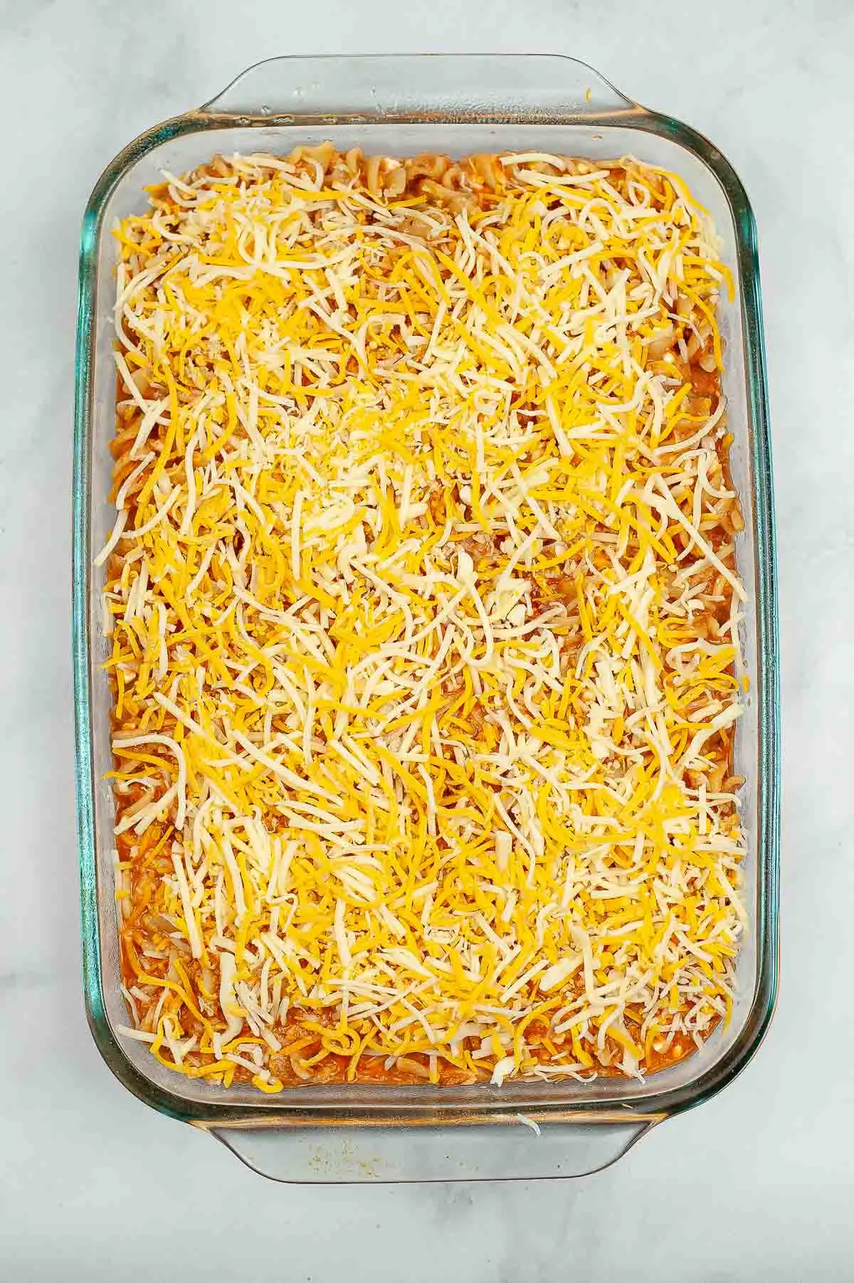 Pasta mixed with sauce and ricotta topped with shredded cheese in a baking dish.