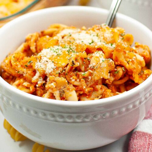 Bowl of cheesy rotini with pasta sauce and cheese on top.