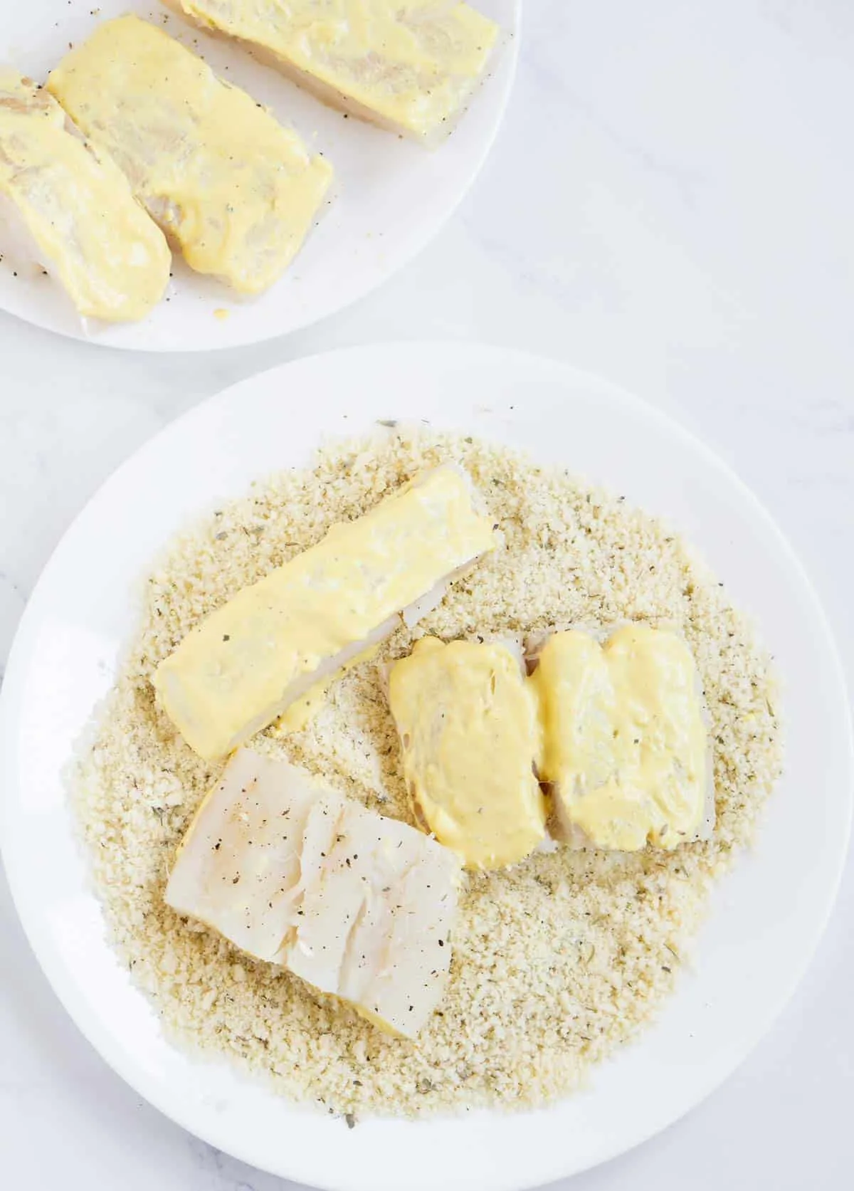 Cod fillets brushed with mustard and mayo being dipped into the panko mixture.