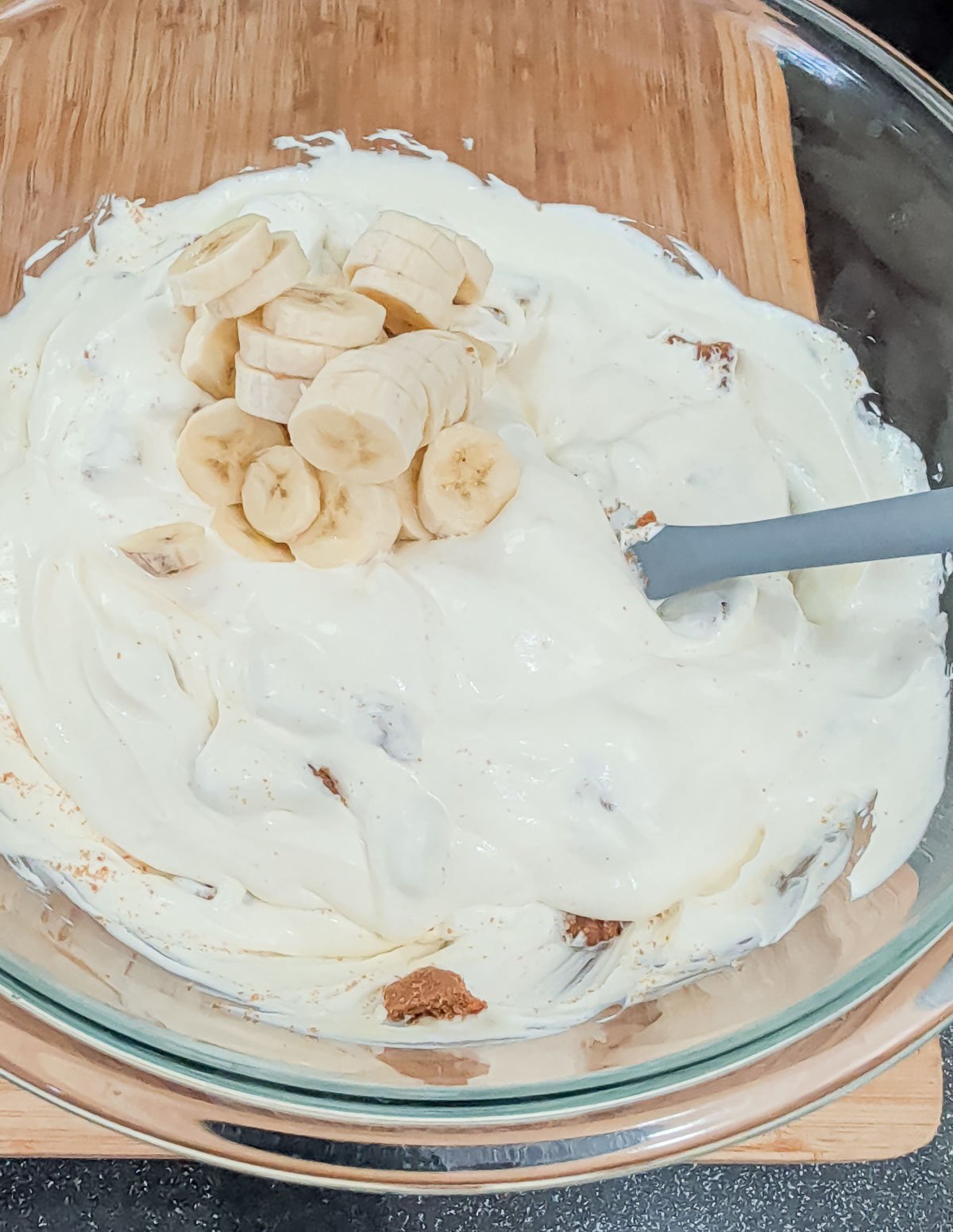 folding sliced bananas and biscoff cookies into banana pudding