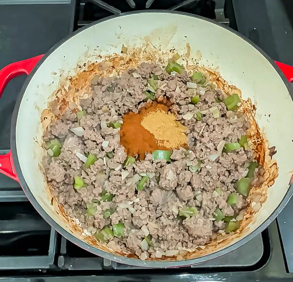 Adding chili powder and ground cumin to browned ground venison in a soup pot