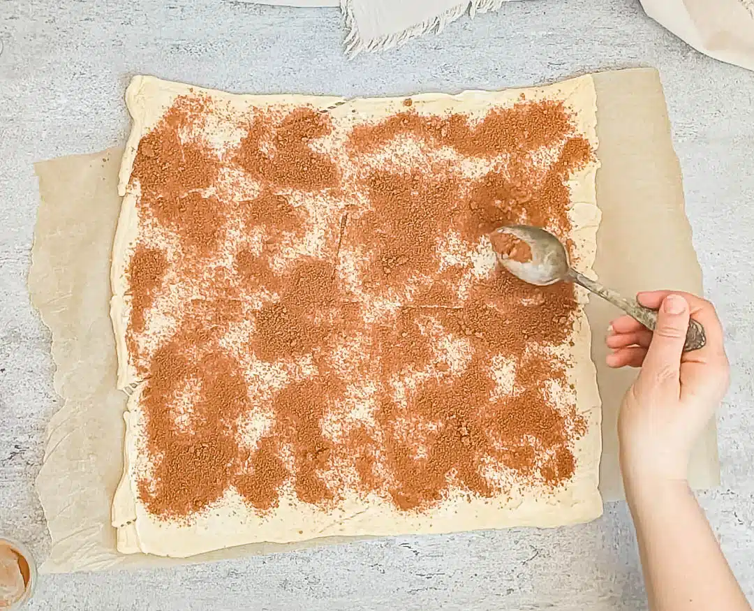 Sprinkling cinnamon sugar on buttered crescent roll dough