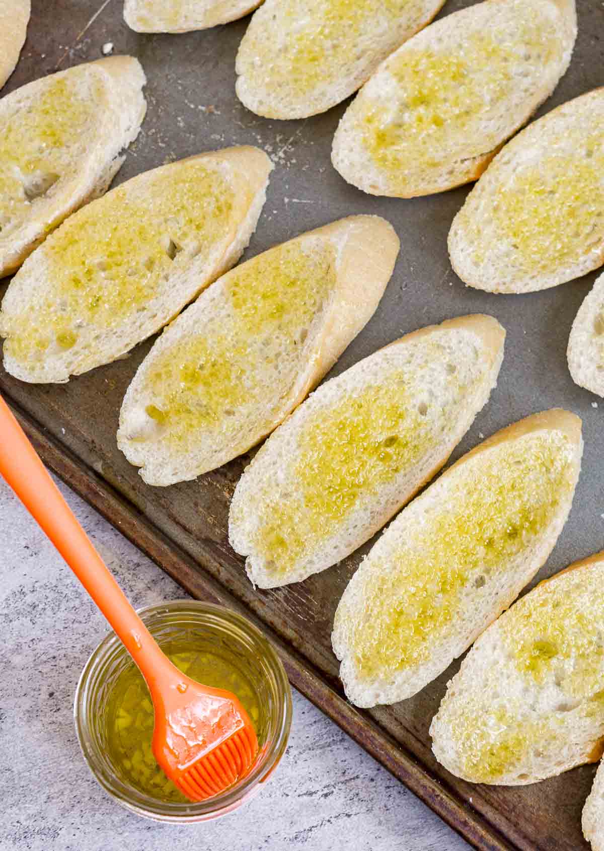 Brushing garlic-infused olive oil on baguette slices