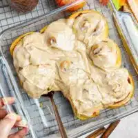Hand taking out an apple butter cinnamon roll from a baking pan